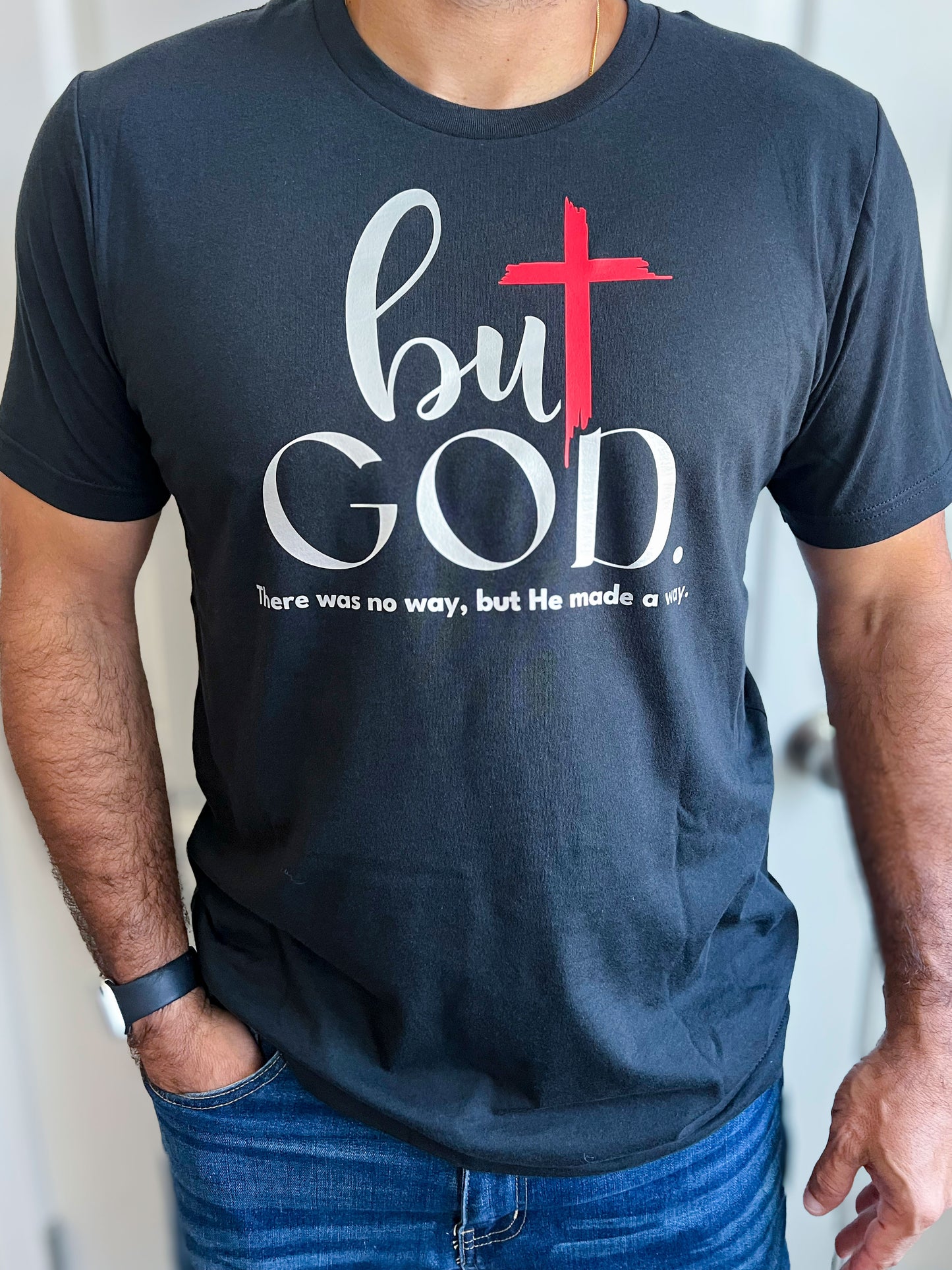 Man wearing a vintage black T-shirt with ‘but GOD.’ in bold silver script, featuring a red cross as part of the design. Below, the phrase ‘There was no way, but He made a way.’ is printed in small white text. Styled with blue jeans.